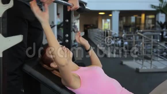 健身女士在健身房的教练监督下做杠铃凳视频的预览图
