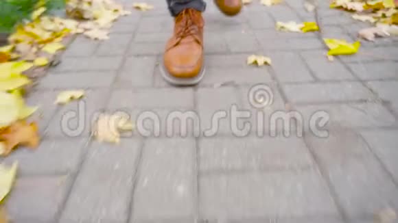 一个穿皮鞋的年轻人走在一条有落叶的人行道上视频的预览图
