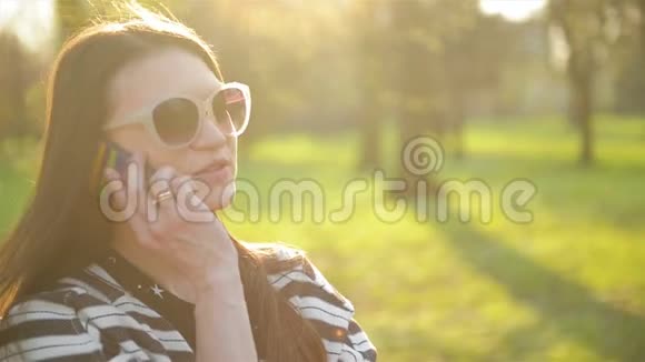 智能手机户外美女画像头发长戴着彩色太阳镜的布鲁内特微笑视频的预览图