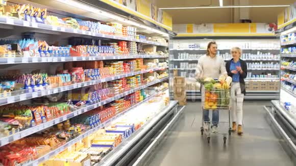 男性和女性购物者用超市过道上的食品推车视频的预览图
