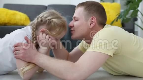 照顾家庭中的孩子爸爸亲吻拥抱一个小女儿躺在客厅的地板上视频的预览图
