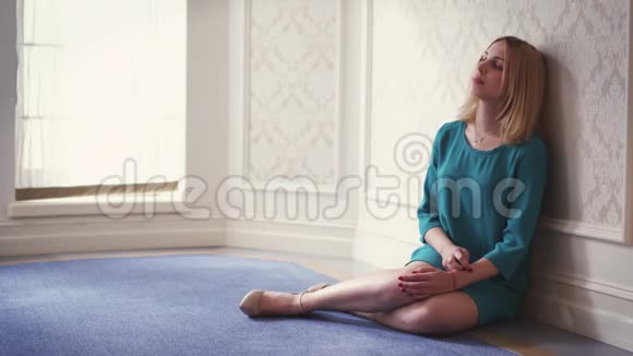 坐在地板上靠着墙靠近窗户的灯光房里沉思的女人视频的预览图