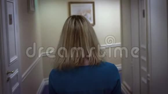 酒店的走廊上走着一位身穿蓝色裙子的年轻金发女子视频的预览图