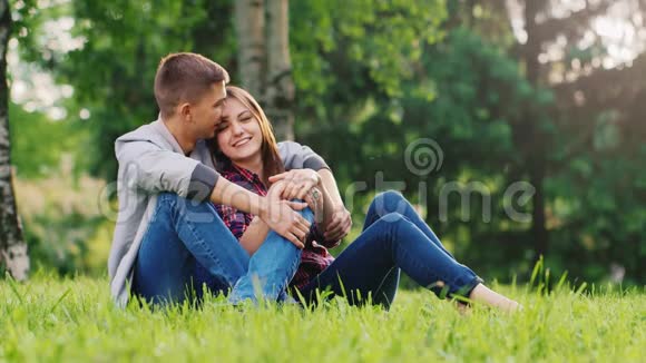 一对相爱的夫妇在公园里休息坐在草坪上的怀抱里交谈视频的预览图
