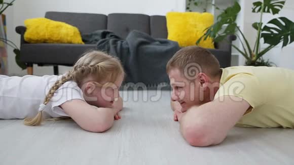 快乐的现代家庭爸爸和他的小女儿躺在客厅的地板上互相看着视频的预览图