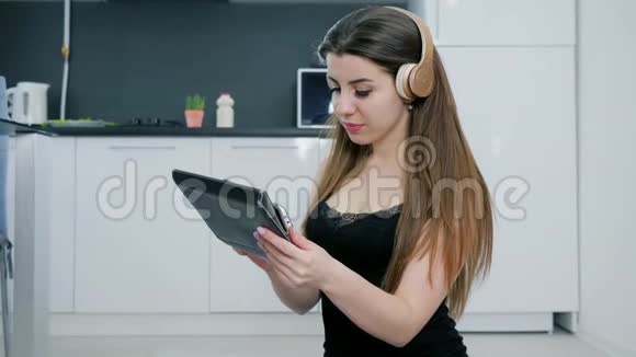 戴耳机的女孩在厨房里用平板电脑在地上听音乐视频的预览图