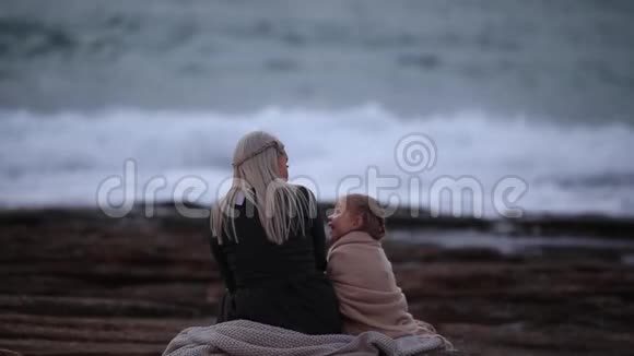 黄昏时分金发女子与小女孩在岩石海岸线上的格子地拥抱视频的预览图