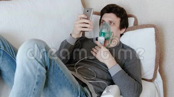 使用雾化器和吸入器进行治疗年轻人通过吸入面罩吸入躺在沙发上聊天视频的预览图