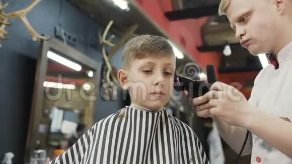 专业理发师在山脊和电动剃须刀的帮助下做了一个新的理发漂亮的男孩和造型师视频的预览图