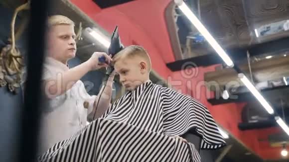 理发师在理发店和理发店里用梳子和吹风机为一个小男孩做发型视频的预览图
