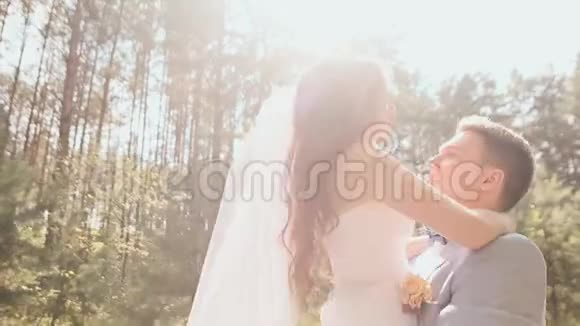 新娘和新郎在森林里摆姿势年轻的新郎高兴地举起新娘把她圈在阳光下视频的预览图