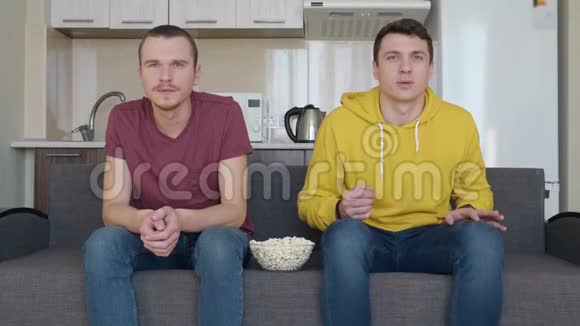 两个男人坐在沙发上看电视上的足球赛吃着爆米花视频的预览图