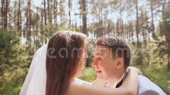 新娘和新郎在森林里摆姿势年轻的新郎高兴地举起新娘把她圈在阳光下视频的预览图