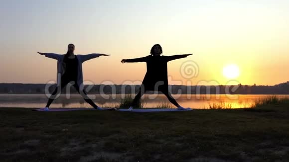 两位年轻女性练习瑜伽并在日落的湖岸左转视频的预览图