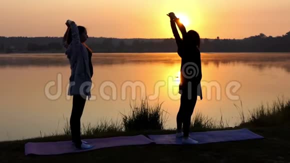 怀孕少女与教练一起在日落湖上做瑜伽运动视频的预览图
