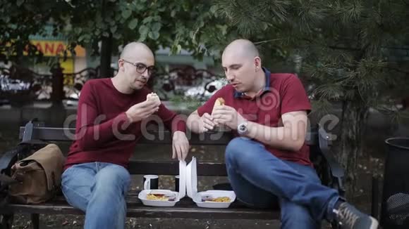 两个男人在公园的长椅上吃午饭吃三明治喝杯子视频的预览图