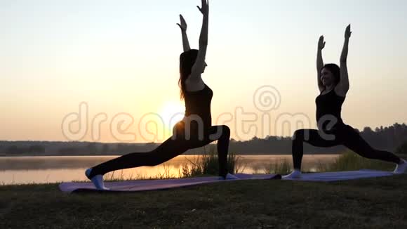 两个瘦女人在斯隆莫的湖岸日落时做瑜伽勇士运动视频的预览图