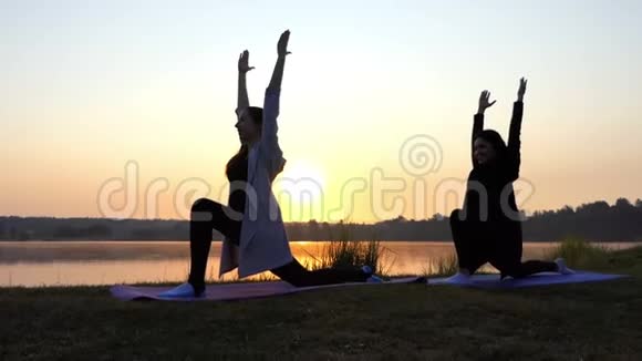 两位年轻女性在斯隆莫夕阳下的美丽湖岸上做瑜伽和微笑视频的预览图