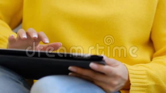 特写镜头年轻女性坐在家里的沙发上使用数字平板电脑浏览互联网和在平板电脑上观看视频视频的预览图