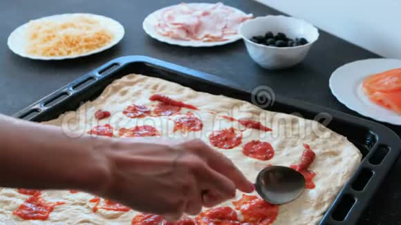 特写镜头中女人的手在披萨面团上撒上酱汁然后用勺子抹上视频的预览图