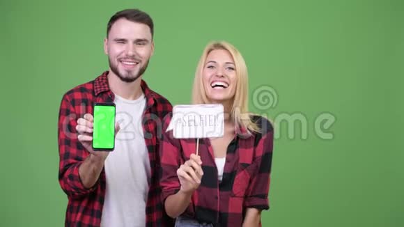 年轻夫妇拿着一张自拍纸签一边看手机视频的预览图