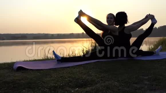 两名年轻女子在斯洛莫日落时分背靠背坐在垫子上练习瑜伽视频的预览图