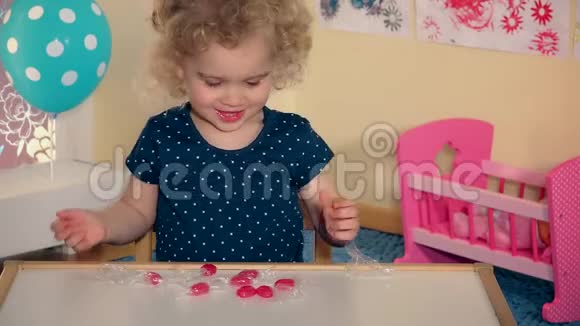情绪化的小女孩在她的小桌子上玩糖果视频的预览图