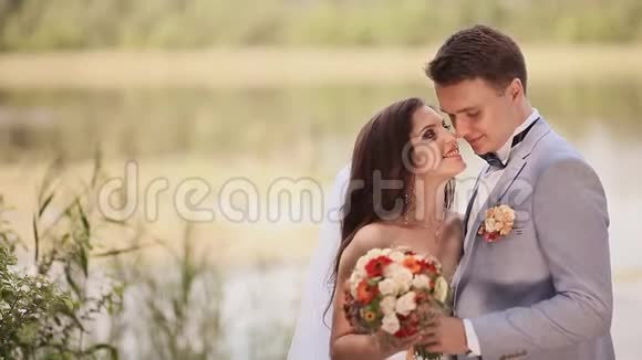 美丽的新娘和新郎一起在湖边的大自然上他们互相拥抱温柔地看着眼睛视频的预览图