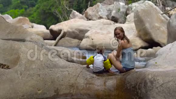 母亲和儿子坐在热带大石头的河流上视频的预览图
