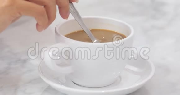 一杯咖啡年轻的亚洲白人女子用手把咖啡和金属勺子混合在一起视频的预览图