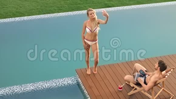 性感的女人在游泳池附近的手机上拍照现代夫妇度假休闲视频的预览图