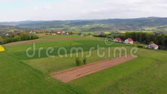 在一个有小房子的村庄里空中无人机可以看到绿田丘陵和树木波兰视频的预览图