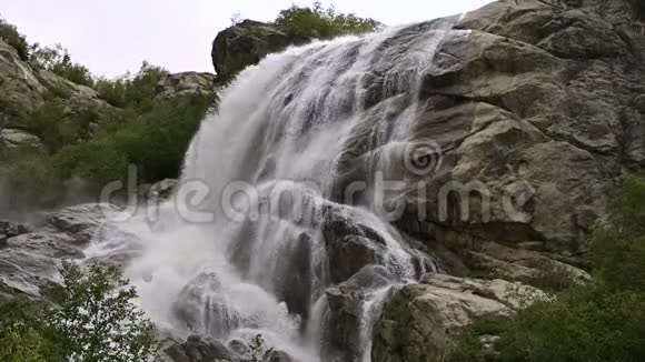 慢动作的水从一块巨大的岩石上掉下来阴天有小雨的自然环境中的瀑布视频的预览图