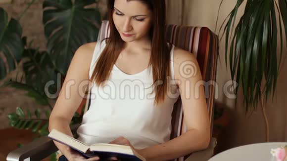 年轻漂亮的女孩坐在椅子上看书一个女人在业余时间聚精会神地看书快关门视频的预览图