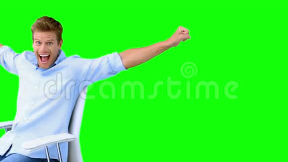 一个人坐在转椅上举起双臂展示他在绿色屏幕上的成功视频的预览图