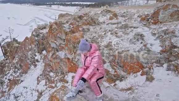 女人坐在山上旅行者正在山顶上散步漂亮的女孩穿着时尚的粉红色羽绒服视频的预览图