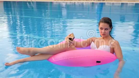 穿泳装的女孩在电话上拍照在度假时在游泳池边游泳进入充气圈视频的预览图