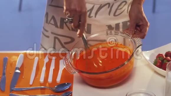 女人她的手在白色桌子上的大玻璃碗里搅动着橙色的物质视频的预览图