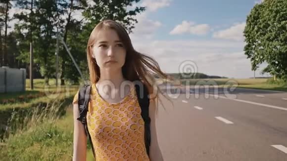 年轻漂亮的俄罗斯女孩长发穿着一件连衣裙背着一个背包正在高速公路上追赶一辆车她是视频的预览图