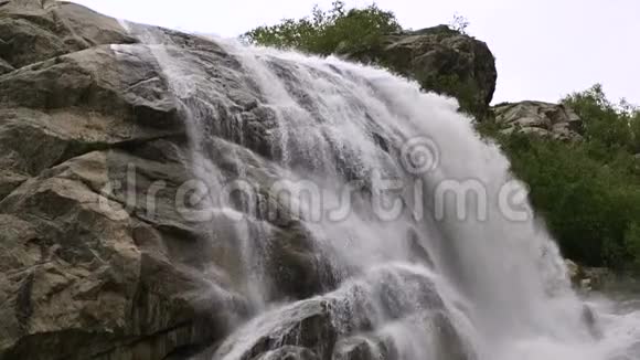 慢动作的水从一块巨大的岩石上掉下来阴天有小雨的自然环境中的瀑布视频的预览图