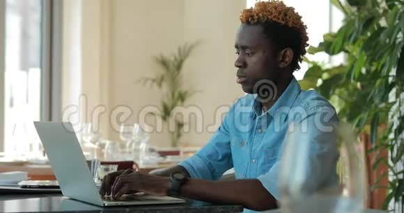 使用笔记本电脑的非裔美国人用手机在咖啡馆打电话视频的预览图