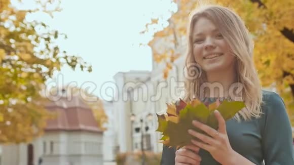 穿着裙子的年轻迷人的女孩正在公园里享受秋天她捧着一束秋叶视频的预览图