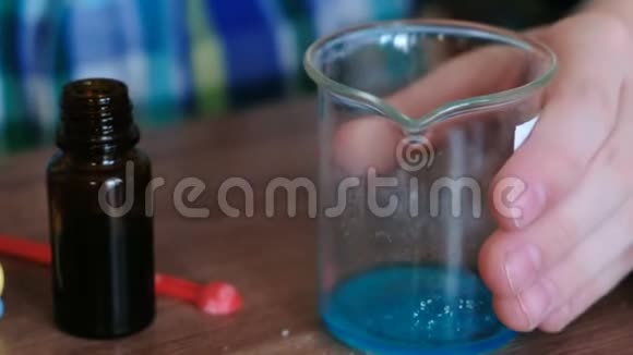 家庭化学实验特写男孩用玻璃把物质和蓝色液体混合在烧杯里视频的预览图