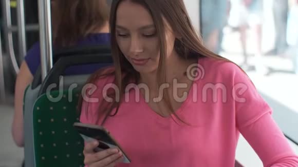 年轻快乐的女人在旅行中坐在靠近窗户的公共交通工具上使用智能手机视频的预览图