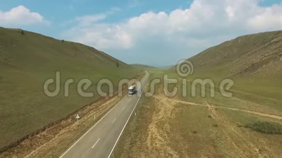 在阳光明媚的一天在公共汽车和汽车的上方沿着空乡村道路在山丘之间行驶视频的预览图
