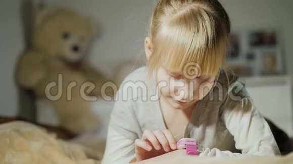 一个女孩正在玩她手臂上的智能时钟躺在卧室的床上视频的预览图