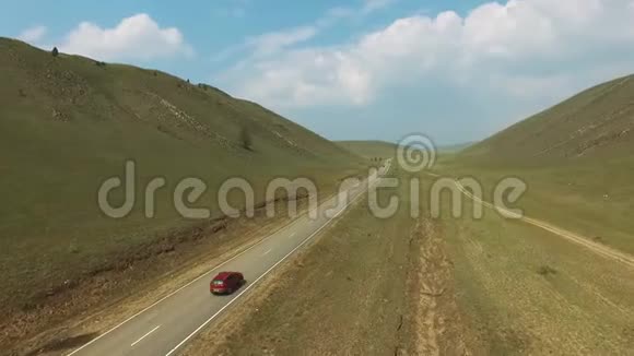 在阳光明媚的一天汽车沿着空乡村道路行驶在山丘之间的空中视野视频的预览图