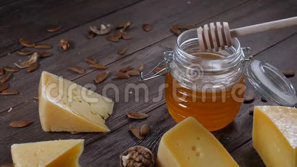 奶酪和蜂蜜各种各样的硬奶酪都在木制背景上蜂蜜在蜂蜜棒上慢动作视频的预览图