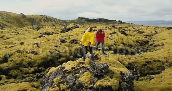 两个女人站在岩石上一起徒步旅行的鸟瞰图科普特在冰岛的熔岩田里飞来飞去视频的预览图