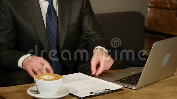 咖啡馆里的商人用商业文件工作男人坐在咖啡馆的桌子旁笔记本电脑和咖啡躺在桌子上视频的预览图
